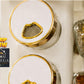 Decorative jars with gold lids on a white surface, featuring the Omega brand.
