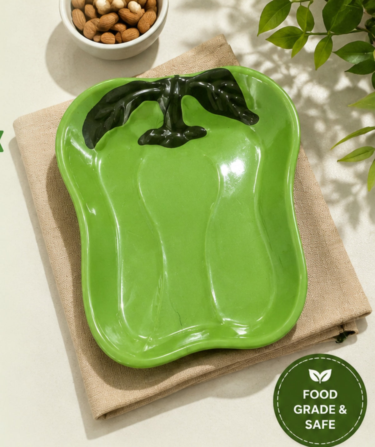 Green ceramic pepper-shaped dish on a beige cloth with a bowl of nuts in the background.