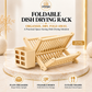 Omega Shop foldable dish drying rack in a light natural wood finish, shown open with a plate organizer cup on the left. The product is displayed on a round marble pedestal with promotional text and feature icons on a warm beige background.